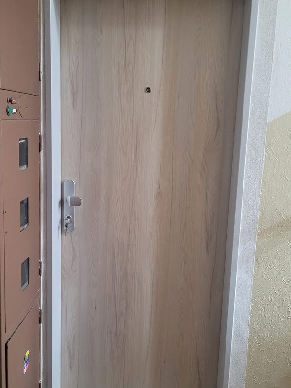 Bezpečnostné dvere FORNOX vo svetlom drevodekore osadené na chodbe paneláka