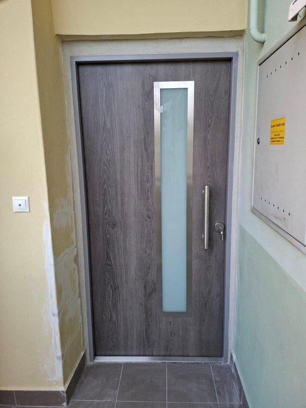 Bezpečnostné dvere FORNOX v sivom dube s presklením a madlom osadené vo vchode